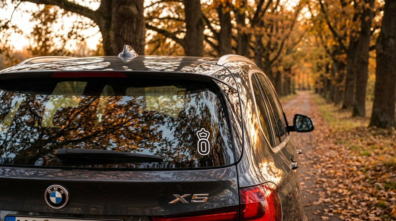 Oldenburg registry vinyl sticker on a charcoal BMW X5 on an autumn oak-lined lane, warmblood breed sticker decal