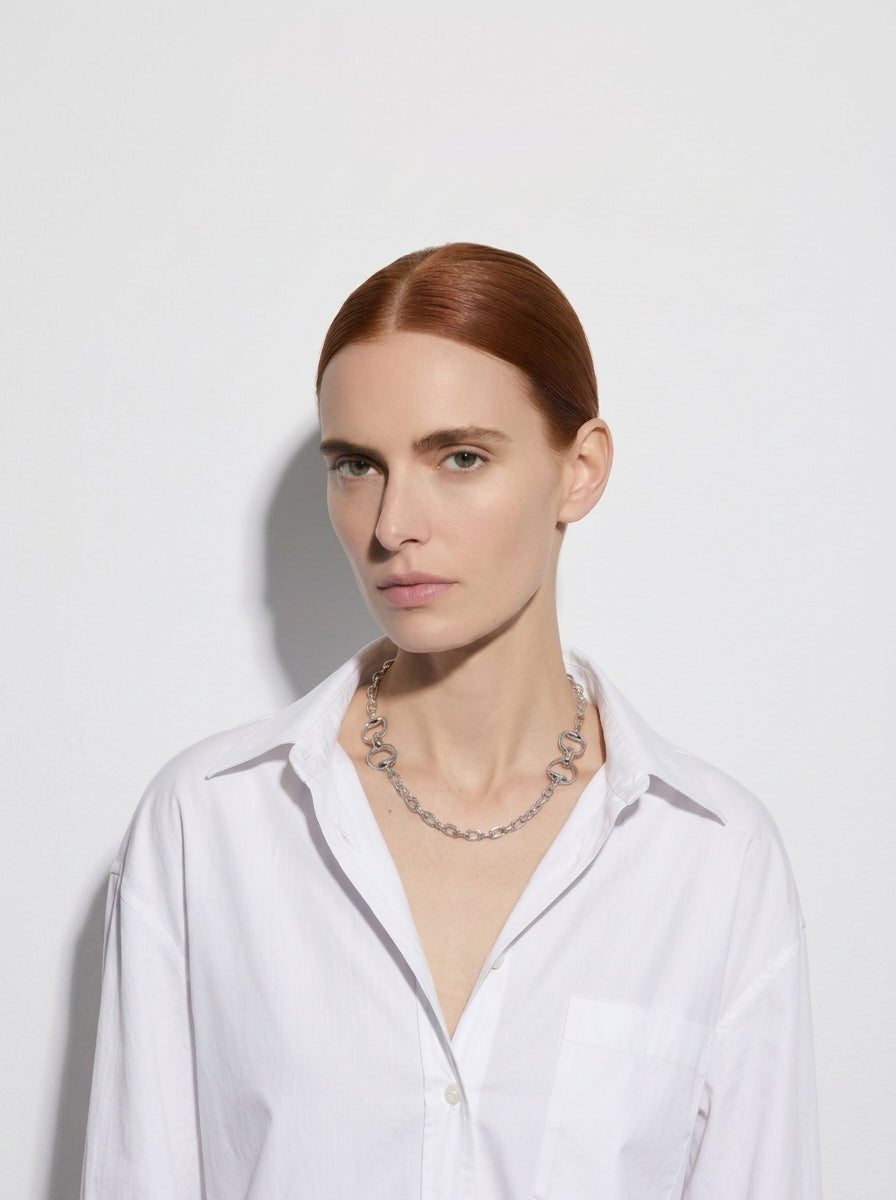 Woman wearing a white shirt and silver necklace against a light gray background