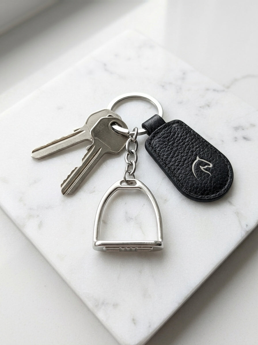 Keychain with horse stirrup charm and black leather case on marble surface
